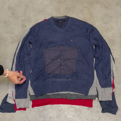 Gestapelde Tommy Hilfiger truien in verschillende kleuren op een betonnen vloer, onderdeel van de Sweater Box van Vintagebulk groothandel.